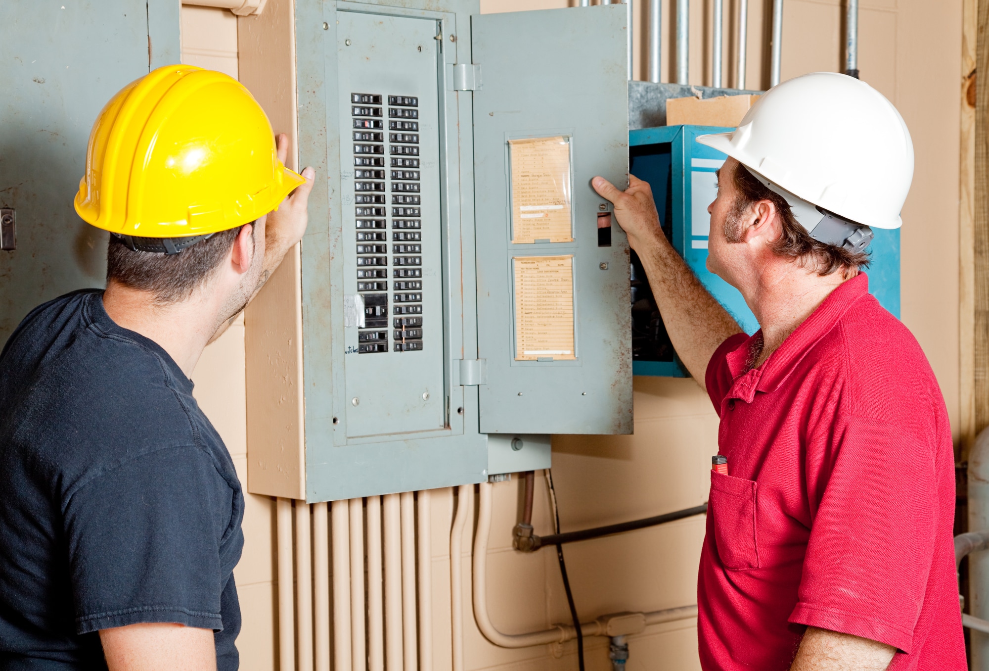 Electricians examining a circuit breaker panel in an industrial setting.